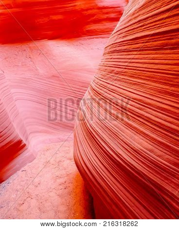 Striations in sandstone lead into curve of path through slot canyon in bright red colors.