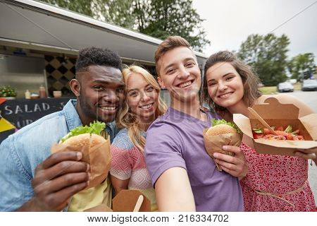 leisure, eating and people concept - happy friends with wok and burgers taking selfie at food truck