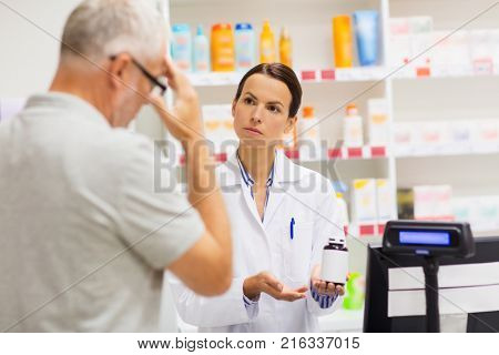 medicine, pharmaceutics, health care and people concept - apothecary showing analgetic drug to senior man customer with headache at drugstore