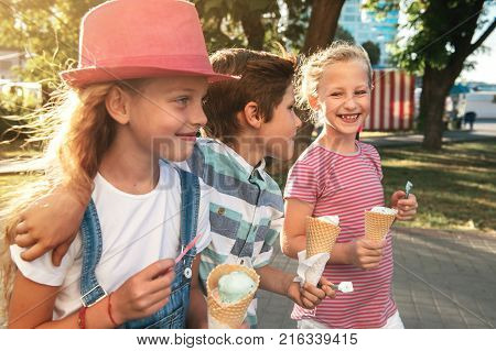 Close-up portrait of three happy preteen children walking on the street having fun and eating ice-cream