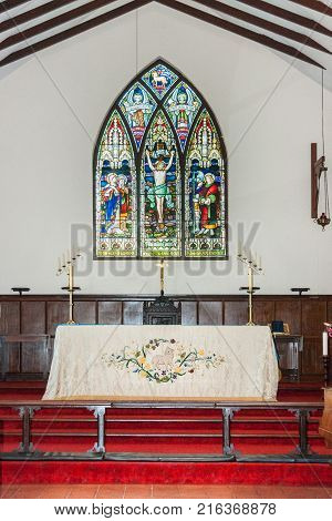 Albany WA Australia - November 23 2009: Chancel and sober altar with cover against colorful stained glass backdrop of Uniting church in Australia. Red carpet white wall dark blue wood furniture.