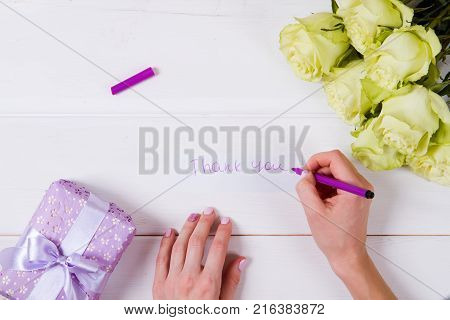 Woman's hand with pen writing on the white blank greeting card on the table. White green roses. Fresh flowers.