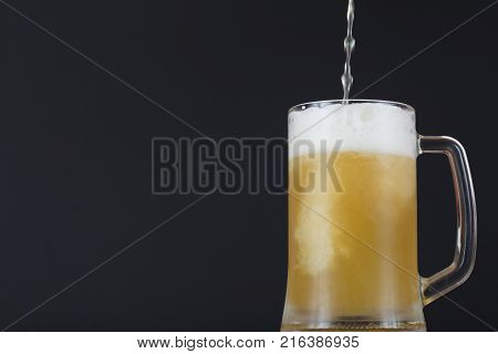 Beer in mug with place for text. A light beer pours into the glass. Unfiltered beer in a misted glass with copy space. Beer is poured into the glass close up.