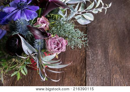 floral design, decor, sentiments concept. there is lovely bouquet made of ballet pink roses, purple anemons, amazing dark maroon persian battercups, embellished with different leaves and thistles