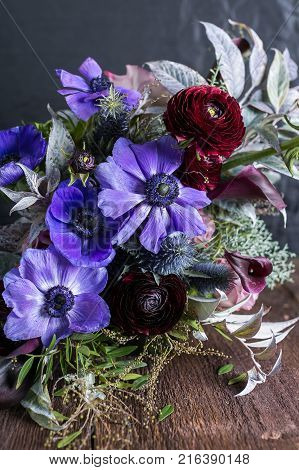 decoration, natural elements, engagement concept. close up of wedding bouquet composed mostly of delicate lilac anemons and puffy dark maroon battercups, so called rununculuses