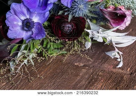flower arranging, wedding, planting concept. on the dark wooden table there is bunch of flowers in various coloures, lilac, maroon, dark pink, all flowers mixed with decorative leaves