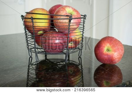 One apple in front of a metal basket filled with red McCoun apples.