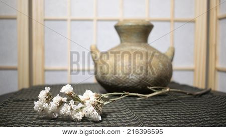 Pottery vase with statice flower in front of shoji on patterned cloth.