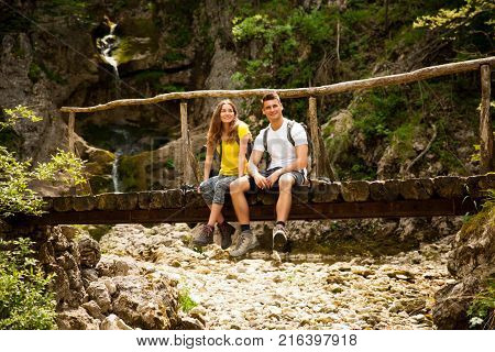 Active Young Cople Hiking On A Wooden Brifge Over Mountain Creek