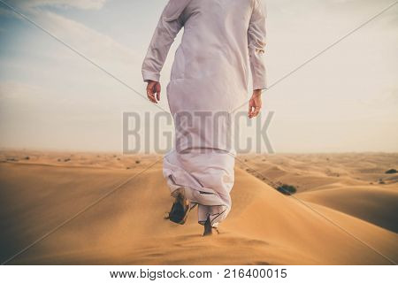 Arabian man walking in the desert at sunrise