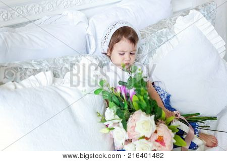 Funny and cute brunette little smiling girl playing on bed in bedroom. White interior with big bed