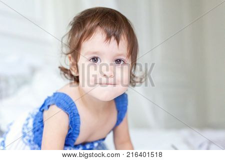 Funny and cute brunette little smiling girl playing on bed in bedroom. White interior with big bed
