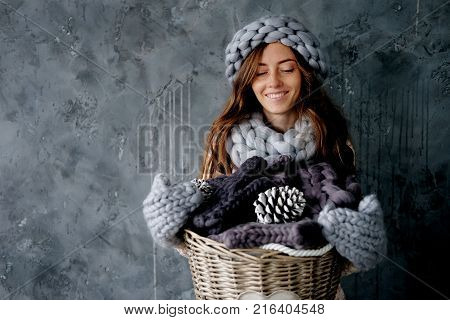 Winter fashion accessories.Young woman dressed for cold weather in grey snood hat and mittens holding a basket full of knitted clothes.