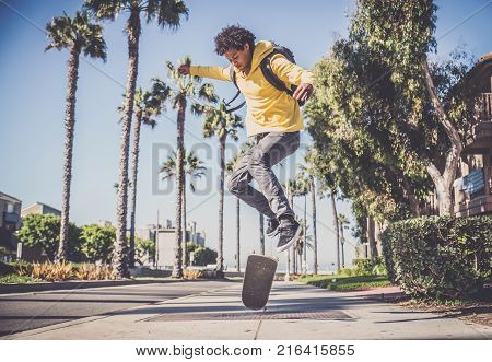 Cool skateboarder outdoors - Afroamerican guy jumping with his skate and performing a trick