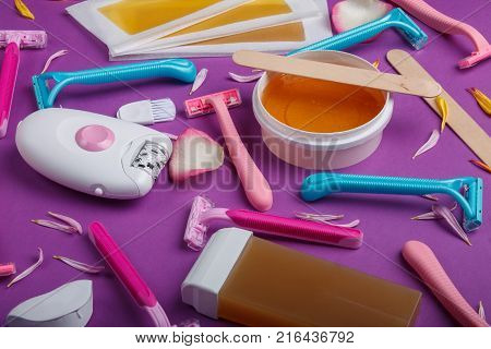 A close-up of a female epilator, disposable razor, wax strips, wax, wax in a cassette, are scattered and lie on a bright pink background.