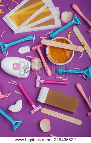 Female epilator, disposable razor, wax strips, wax, wax in a cassette, scattered and lie on a bright pink background, top view.