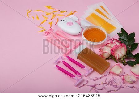 A female epilator and six disposable pink razors, wax strips, wax, wax cachet with roses, lie on a pink background, free space for text.