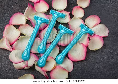 Close-up of four blue disposable razors lie on rose petals, on a gray background. Depilation.