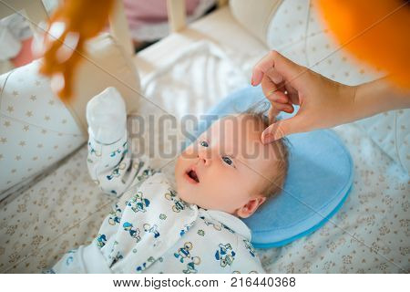 The baby is in a cot in a bright room and looking at toys