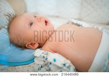 The baby is lying on her back in a cot in a bright room