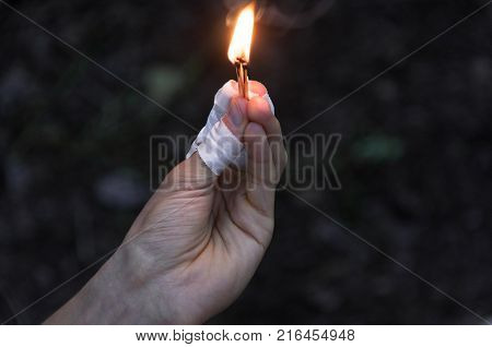 Burning matches in left hand. The flame from the matches pointing to the up. Adult man dark forest background.