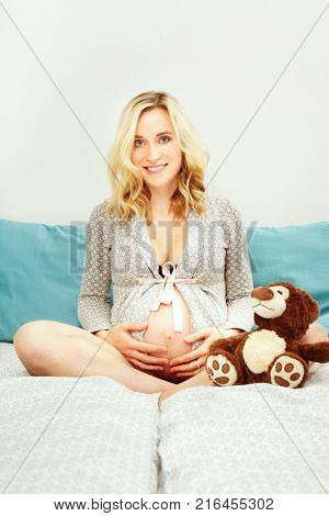 Pregnant young beauty awaiting her newborn while sitting in bed
