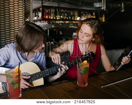 young man learns how to play guitar. tutor shares her skills. help education assistance concept