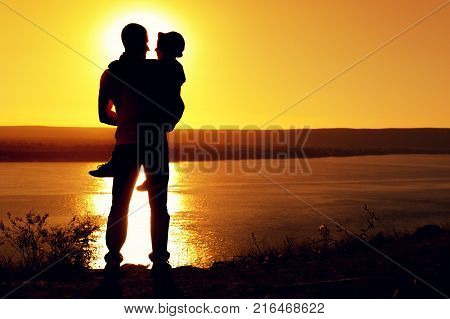 Rear view -  silhouette of the father holding his little son in arms and admiring the sea view on sunny summer evening