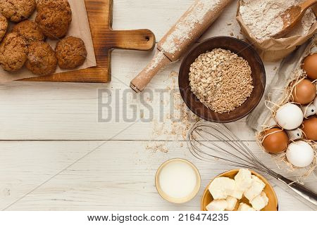 Cooking ingredients for homemade oatmeal cookies. Oat flakes, eggs, butter, milk and kitchen utensils at white rustic background with copy space, top view. Handmade pasty concept and recipe mockup