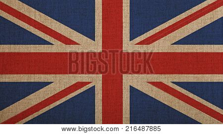 Old grunge vintage dirty faded UK Great Britain national flag over background of jute linen canvas