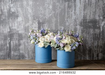 two flower bouquet in a hat box blue. standing on a wooden table. On the background old gray wall art. copy space. blue and white color