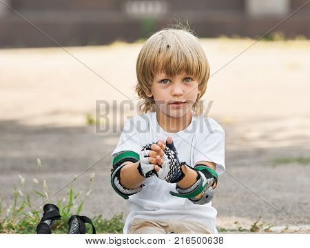 Portrait of little boy taking off gloves after rollerskating