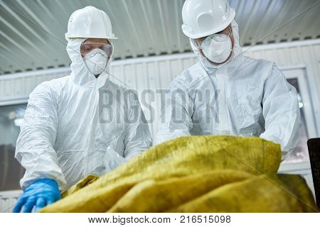 Low angle portrait of two workers  wearing biohazard suits working at waste processing plant sorting recyclable materials on conveyor belt