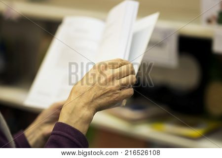 Close-up of hands of the elderly person with open book, bookstore, library. Real scene. Education concept, Self-study, reading fiction, pension, interests in the elderly, life style