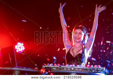 Portrait of active pretty young DJ woman playing music on laser lighting background.