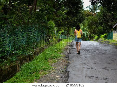 Lady Traveler walking down a road with Greenery