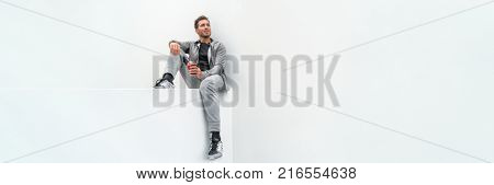 Ftiness sport man drinking smoothie workout banner relaxing at home in gym jogging pants activewear outdoor. Athlete sitting on white background.