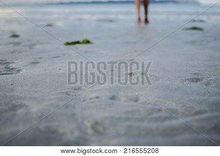 Legs with Footprints on Sand and with a girl walking ahead