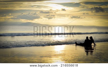 Couple Sitting enjoying beautiful golden sunset on a Beach