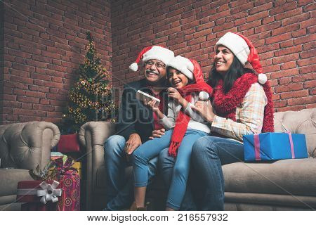 indian grandparents and grand daughter celebrating christmas while watching television and clicking selfie