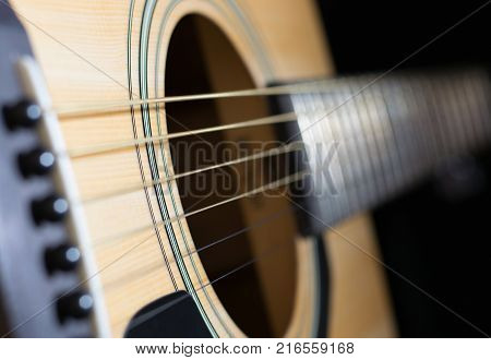 Close-up of rosette and strings of the acoustic guitar on black background.