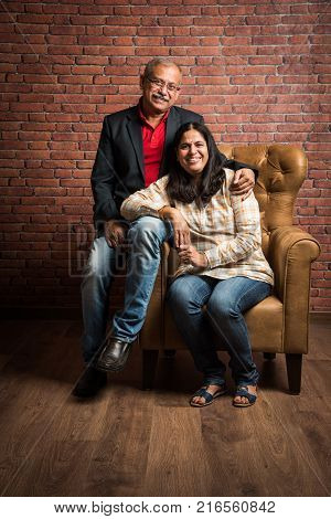 portrait of senior indian couple while sitting on sofa of wing chair