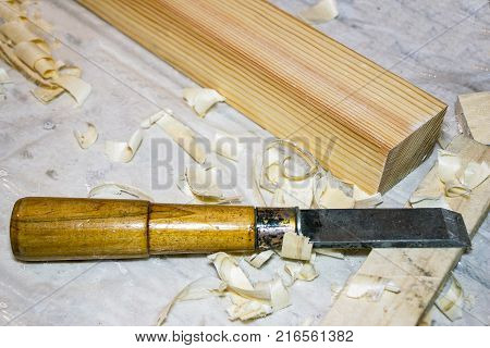 A chisel on the table among the shavings. Nearby there is a wooden bar. Selective focus