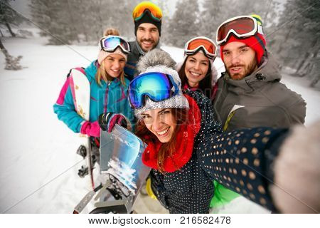 smiling friends having fun on winter hodays. Snowbarders and skiers group team friendship making selfie