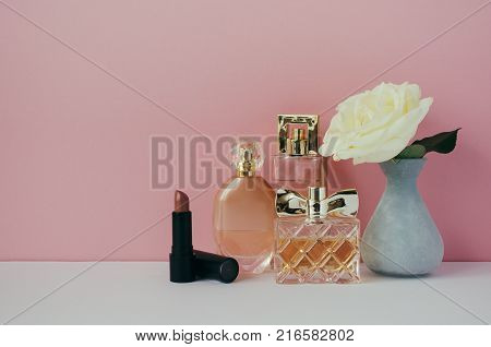 Women's perfume lipstick white rose in a vase on the shelf. Minimalist interior