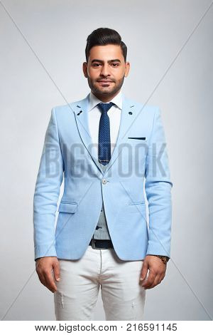 Vertical portrait of a handsome young stylish man wearing white trousers and blue jacket on grey background style fashion confidence masculinity youth concept.