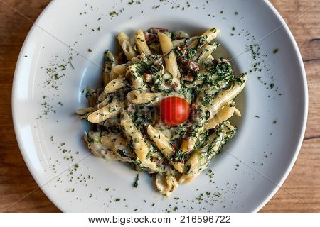 Colorful plate with penne pasta with prosciutto and spinach on a table