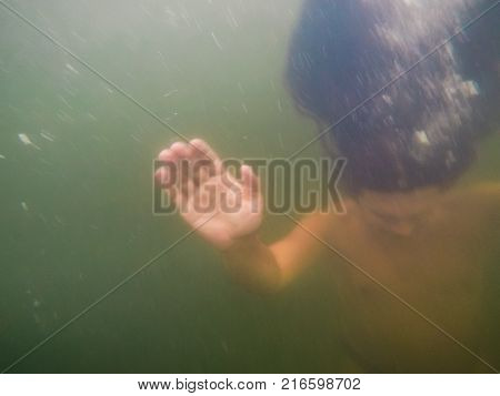 Blurred underwater shot of sinking or drowning person in green turbid water, soft focus, copy space