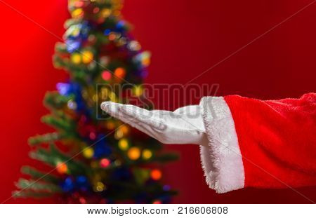 Santa Claus open his hand with decorated Christmas tree on background