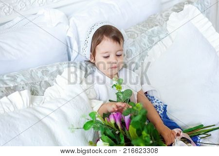 Funny and cute brunette little smiling girl playing on bed in bedroom. White interior with big bed